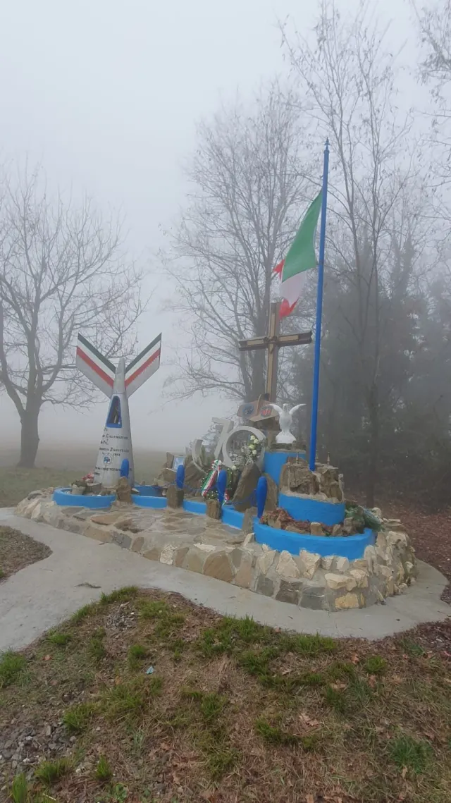 Il monumento ai piloti con le ali tricolori e la croce, avvolto nella nebbia